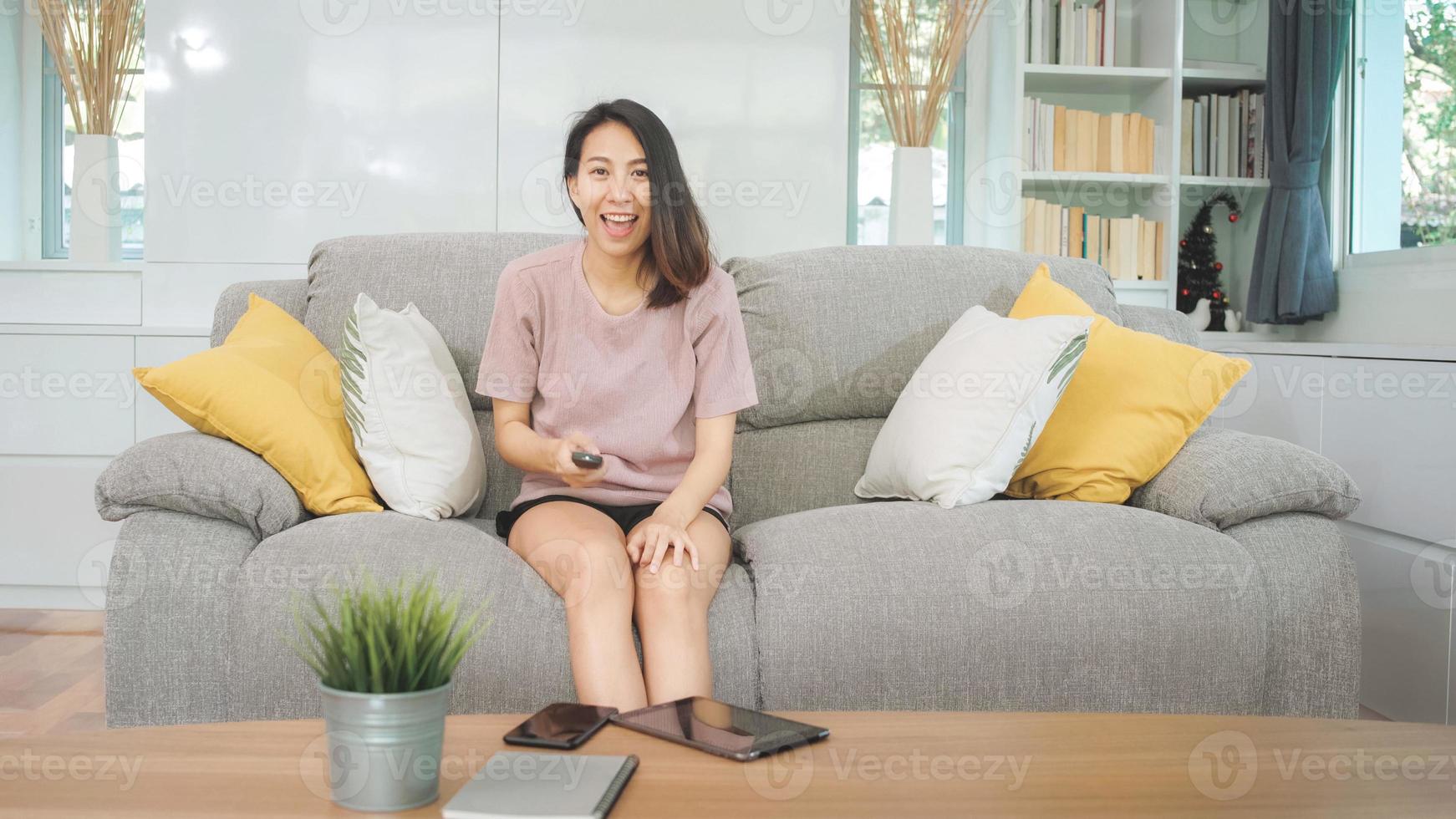 junge asiatische Teenager-Frau vor dem Fernseher zu Hause, weibliches Gefühl glücklich auf dem Sofa im Wohnzimmer liegend. Lifestyle-Frau entspannt sich morgens zu Hause Konzept. foto