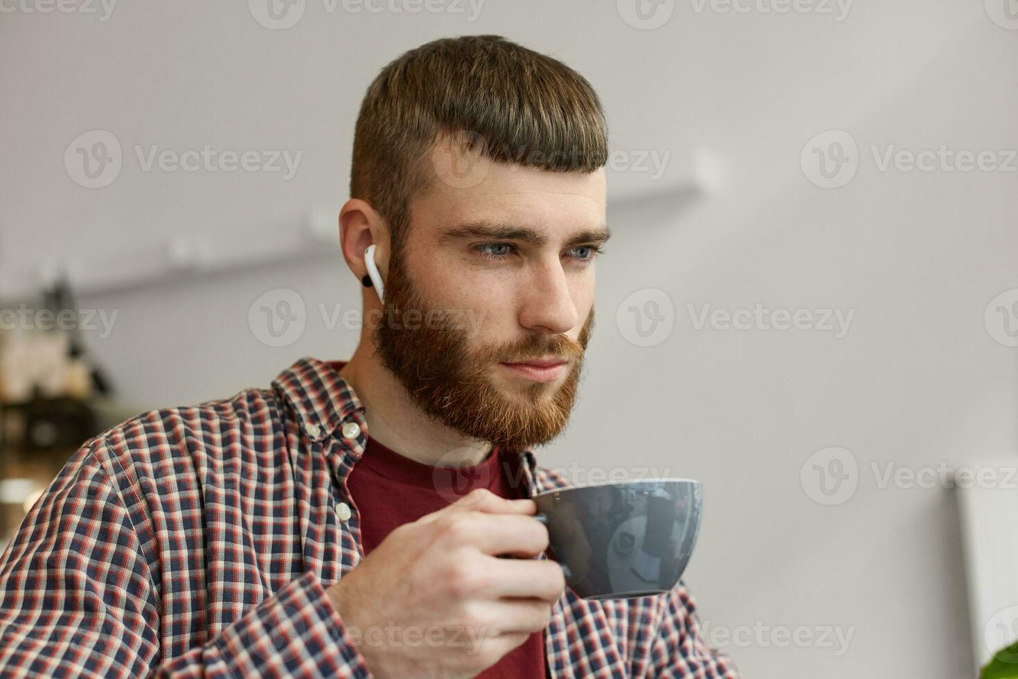 Foto von jung attraktiv Ingwer bärtig Mann halten ein grau Kaffee Tasse, spiegelt auf Pläne zum Morgen und suchen weg, tragen im Basic Kleidung.