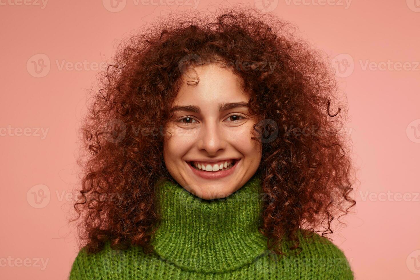 Teenager Mädchen, glücklich suchen Rothaarige Frau mit lockig Haar. tragen Grün Rollkragen Sweatshirt und haben ein hell, warm lächeln. Aufpassen beim das Kamera isoliert, Nahansicht Über Pastell- Rosa Hintergrund foto