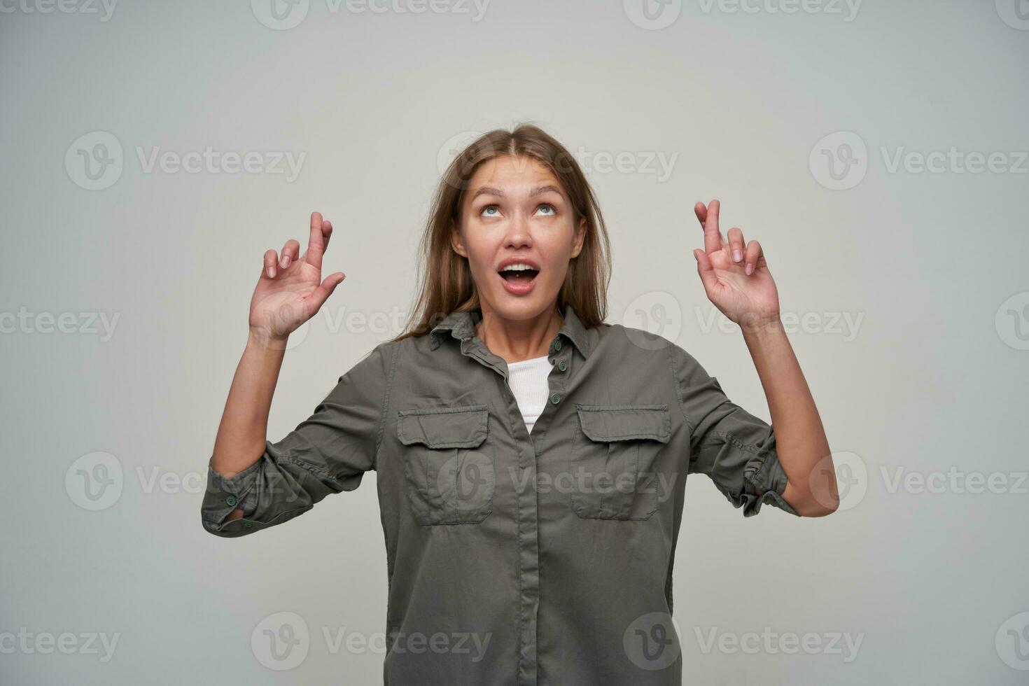 Teenager Mädchen, glücklich suchen Frau mit braun lange Haar. tragen grau Hemd und behalten ihr Finger gekreuzt, Herstellung ein Wunsch, fragen. Aufpassen oben beim Kopieren Raum, isoliert Über grau Hintergrund foto