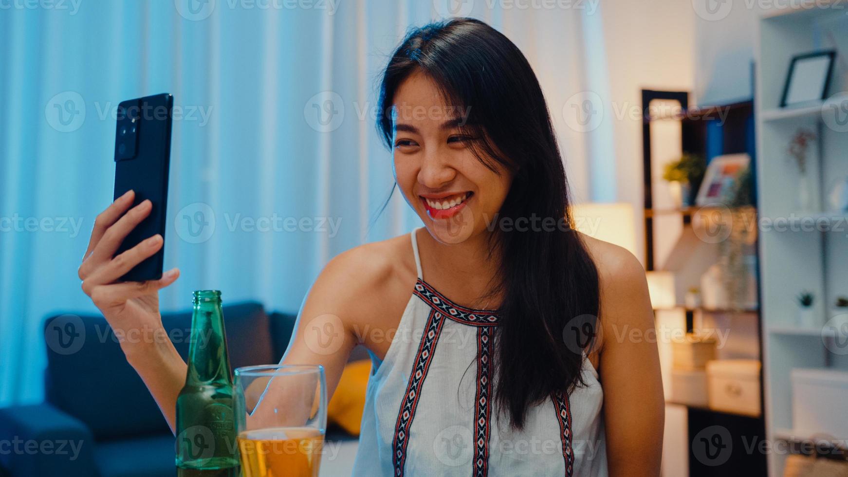 junge asiatische dame trinkt bier und hat spaß fröhliche momentnacht party neujahrsveranstaltung online feier per videoanruf per telefon zu hause nachts. soziale Distanzierung, Quarantäne zur Coronavirus-Prävention. foto
