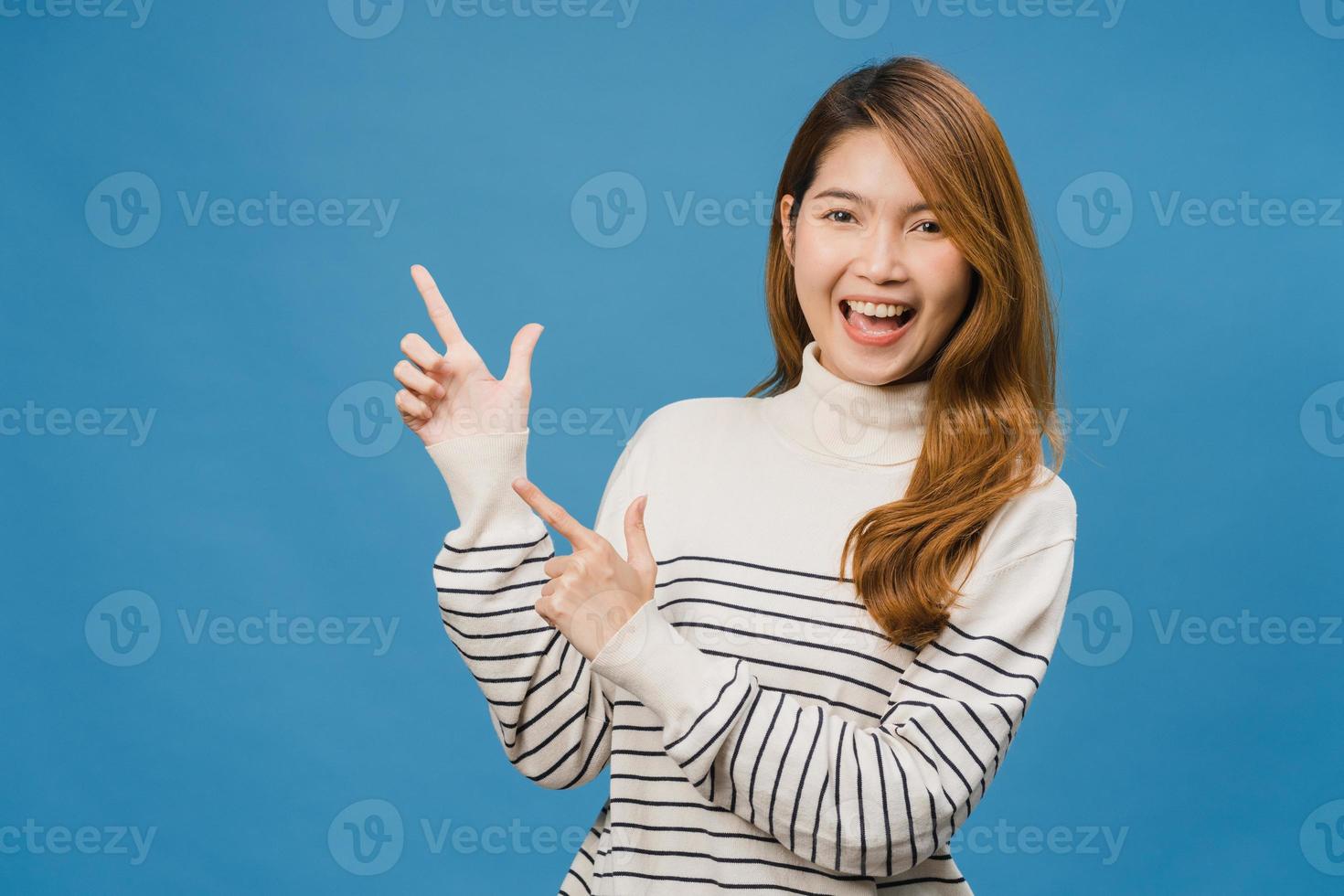 Porträt einer jungen asiatischen Dame, die mit fröhlichem Ausdruck lächelt, zeigt etwas Erstaunliches an leeren Stellen in Freizeitkleidung und blickt auf die Kamera einzeln auf blauem Hintergrund. Gesichtsausdruck Konzept. foto
