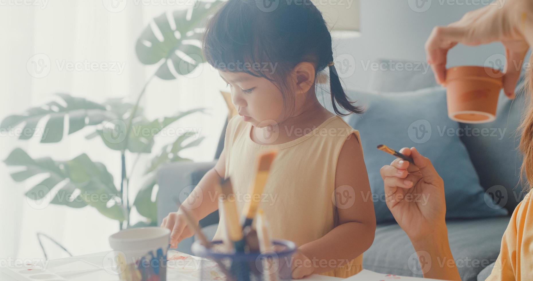 Fröhliche, fröhliche Asien-Familienmutter lehren Kleinkind-Mädchen malen Keramiktopf, der Spaß hat, entspannen Sie sich auf dem Tisch im Wohnzimmer im Haus. Zeit miteinander verbringen, soziale Distanz, Quarantäne zur Coronavirus-Prävention. foto