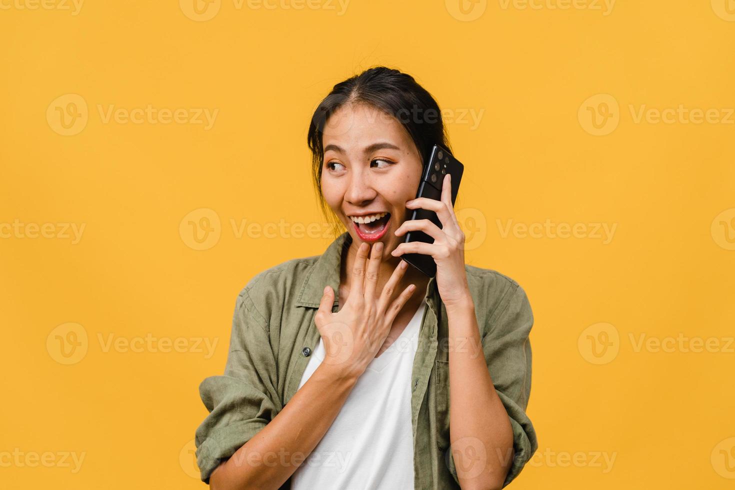 junge asiatische Dame telefoniert mit positivem Ausdruck, lächelt breit, in Freizeitkleidung gekleidet, fühlt sich glücklich und steht isoliert auf gelbem Hintergrund. glückliche entzückende frohe frau freut sich über erfolg. foto