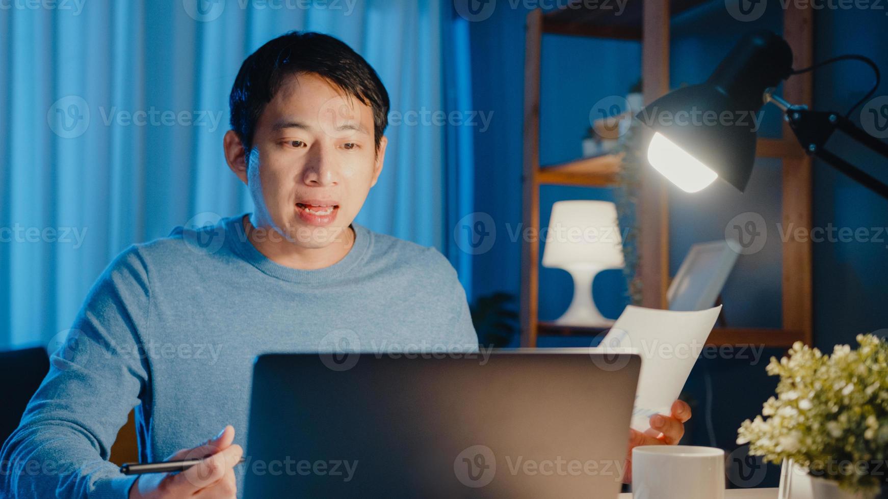 Junger asiatischer Geschäftsmann konzentriert sich auf Online-Videoanruf-Meeting-Aufgaben auf Papierkram mit Kollegen im Laptop-Computer im Wohnzimmer zu Hause Überstunden nachts, Arbeit von zu Hause aus Corona-Pandemie-Konzept. foto