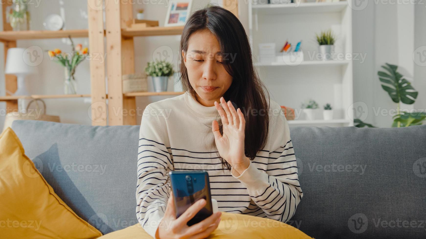 kranke junge asiatische frau hält medizin sitzen auf couch videoanruf mit telefon konsultieren sie mit arzt zu hause. Mädchen nehmen Medikamente nach ärztlicher Verordnung, Quarantäne zu Hause, soziales Distanzierungs-Coronavirus-Konzept. foto