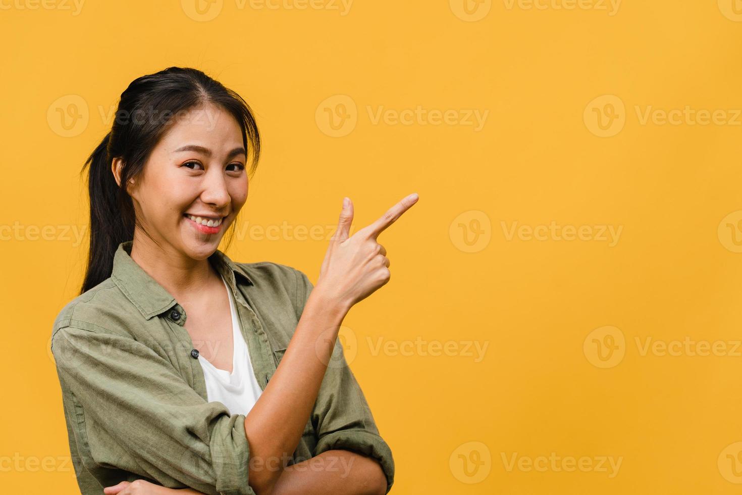 Porträt einer jungen asiatischen Dame, die mit fröhlichem Ausdruck lächelt, zeigt etwas Erstaunliches an leeren Stellen in legerem Tuch und blickt auf die Kamera einzeln auf gelbem Hintergrund. Gesichtsausdruck Konzept. foto