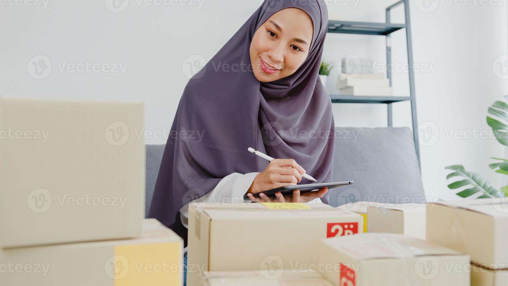 Junge asiatische muslimische Geschäftsfrau Produktbestellung auf Lager überprüfen und auf Tablet-Computerarbeit im Home-Office speichern. Kleinunternehmer, Online-Marktlieferung, Lifestyle-Freelance-Konzept. foto