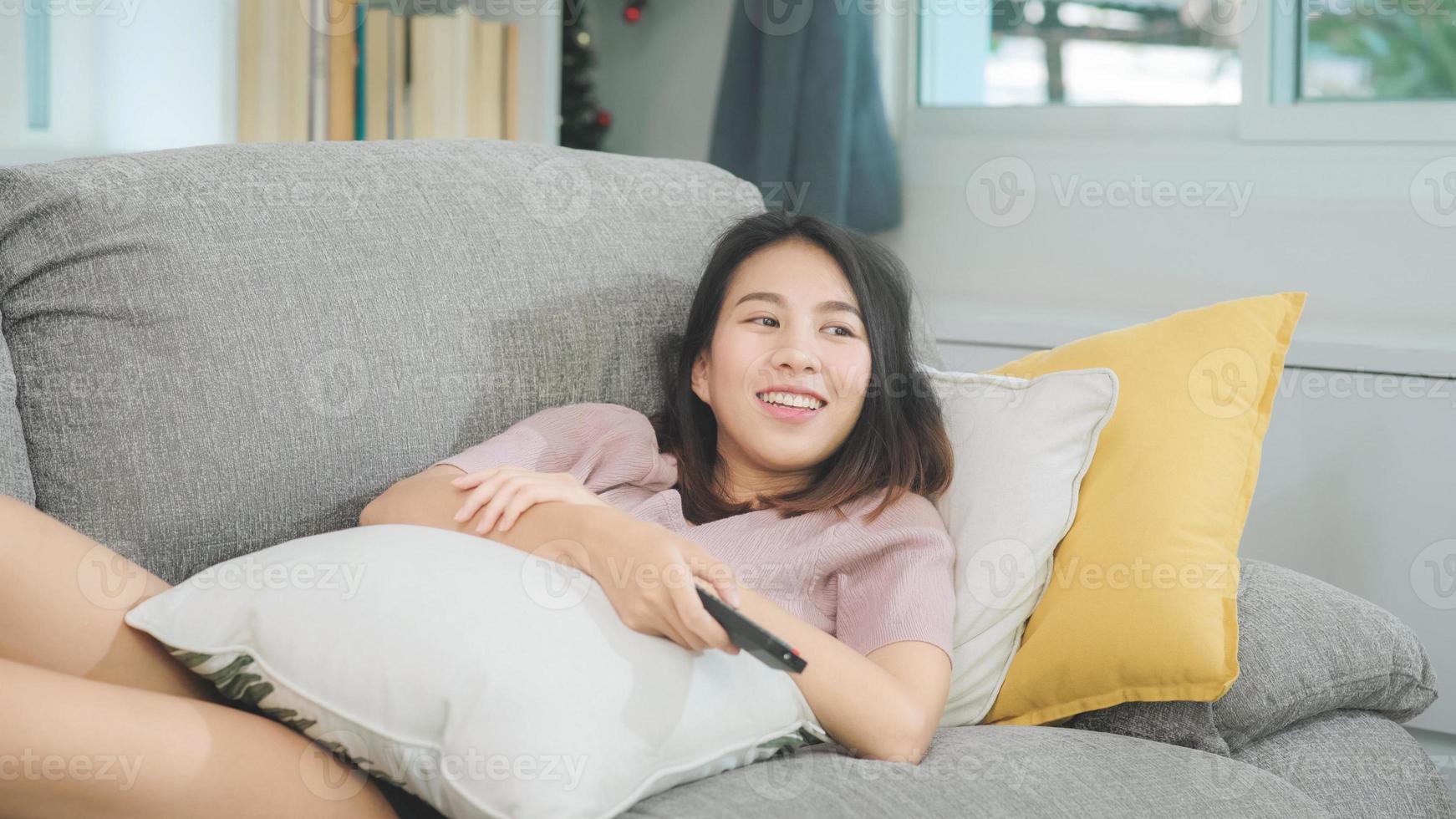 junge asiatische Teenager-Frau vor dem Fernseher zu Hause, weibliches Gefühl glücklich auf dem Sofa im Wohnzimmer liegend. Lifestyle-Frau entspannt sich morgens zu Hause Konzept. foto