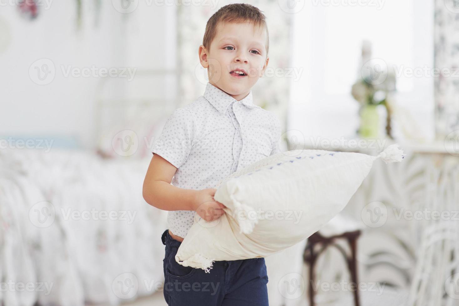 kleiner Junge im weißen Hemd mit Kissen. Kissenschlacht foto