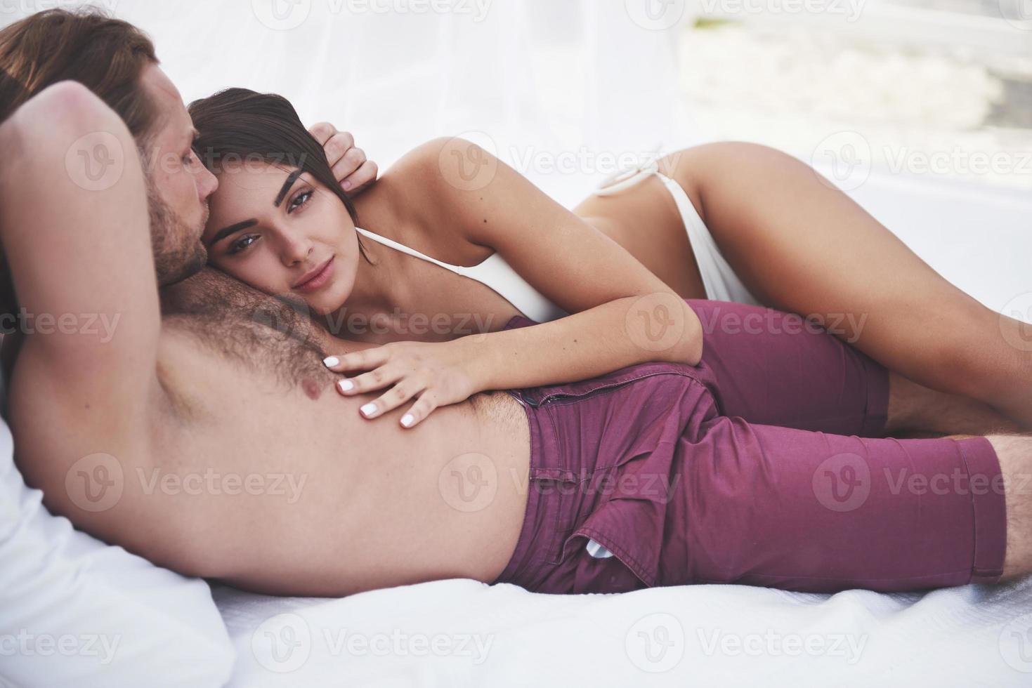 Schönes junges Paar in Badeanzügen am Strand gegen ein Sandlächeln und eine Umarmung. foto