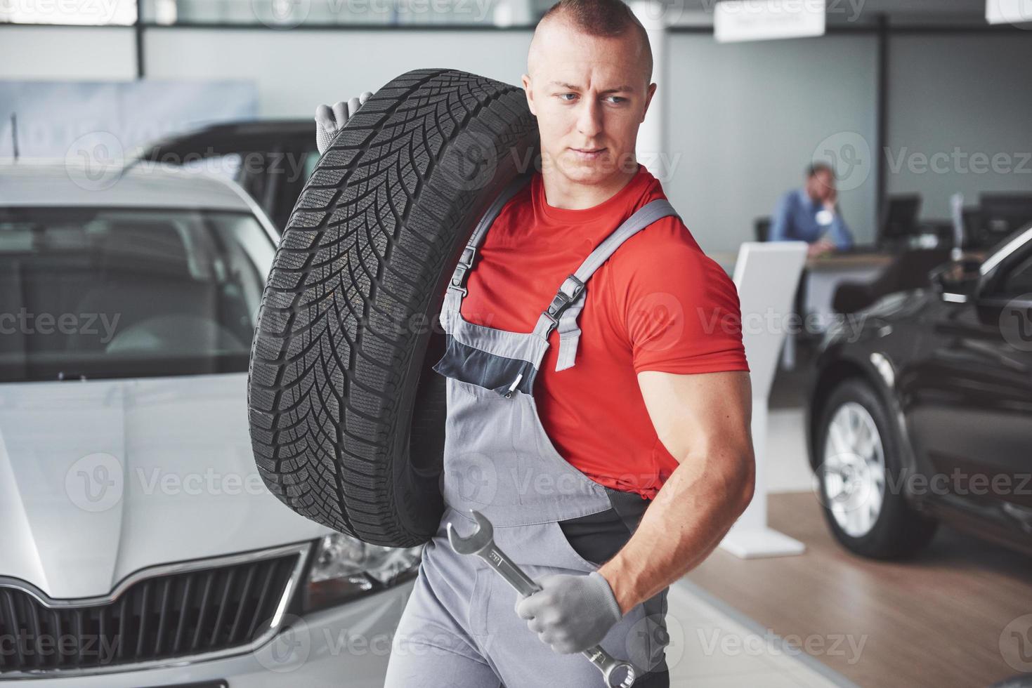 Mechaniker, der einen Reifen in der Werkstatt hält. Wechsel von Winter- und Sommerreifen. foto