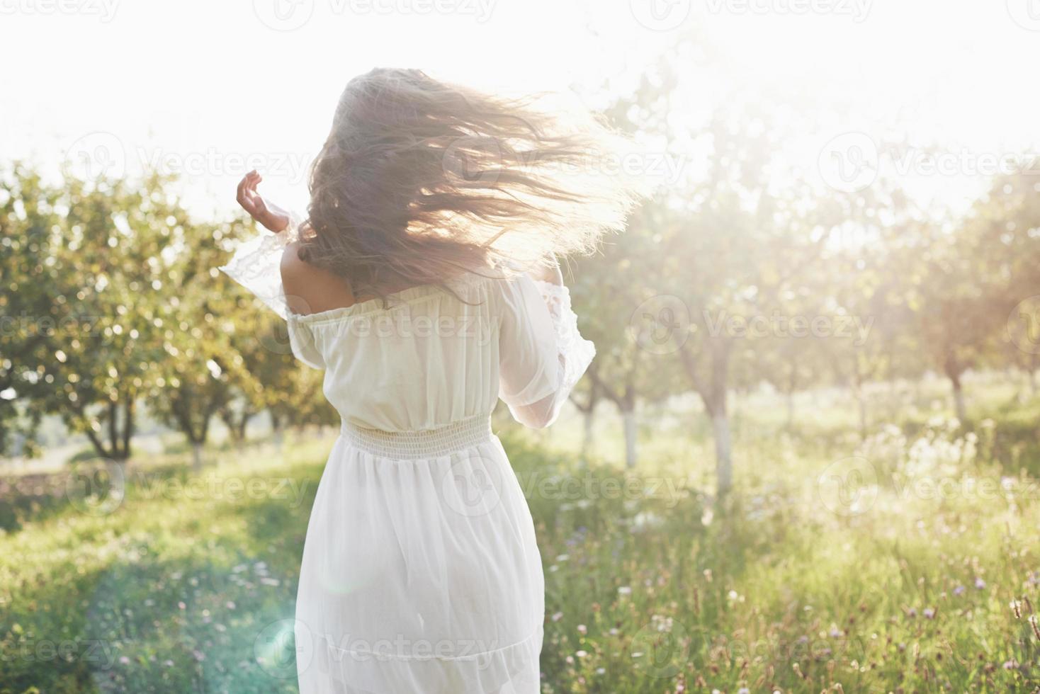 schöne junge frau, die ein elegantes weißes kleid trägt und einen schönen sonnigen nachmittag in einem sommergarten genießt foto