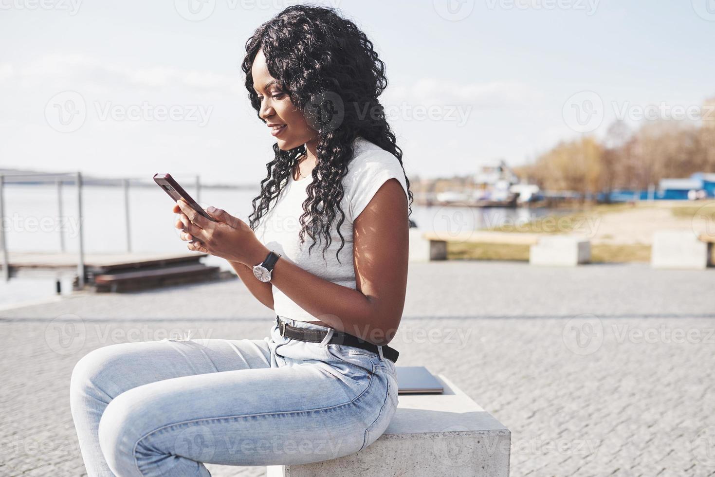 lächelndes schwarzes Mädchen mit einem Telefon am Wasser foto