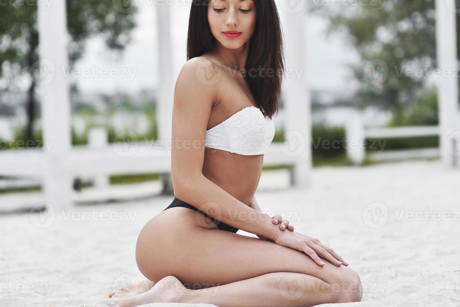 eine schöne frau mit gebräunter haut im badeanzug sitzt auf dem sand foto