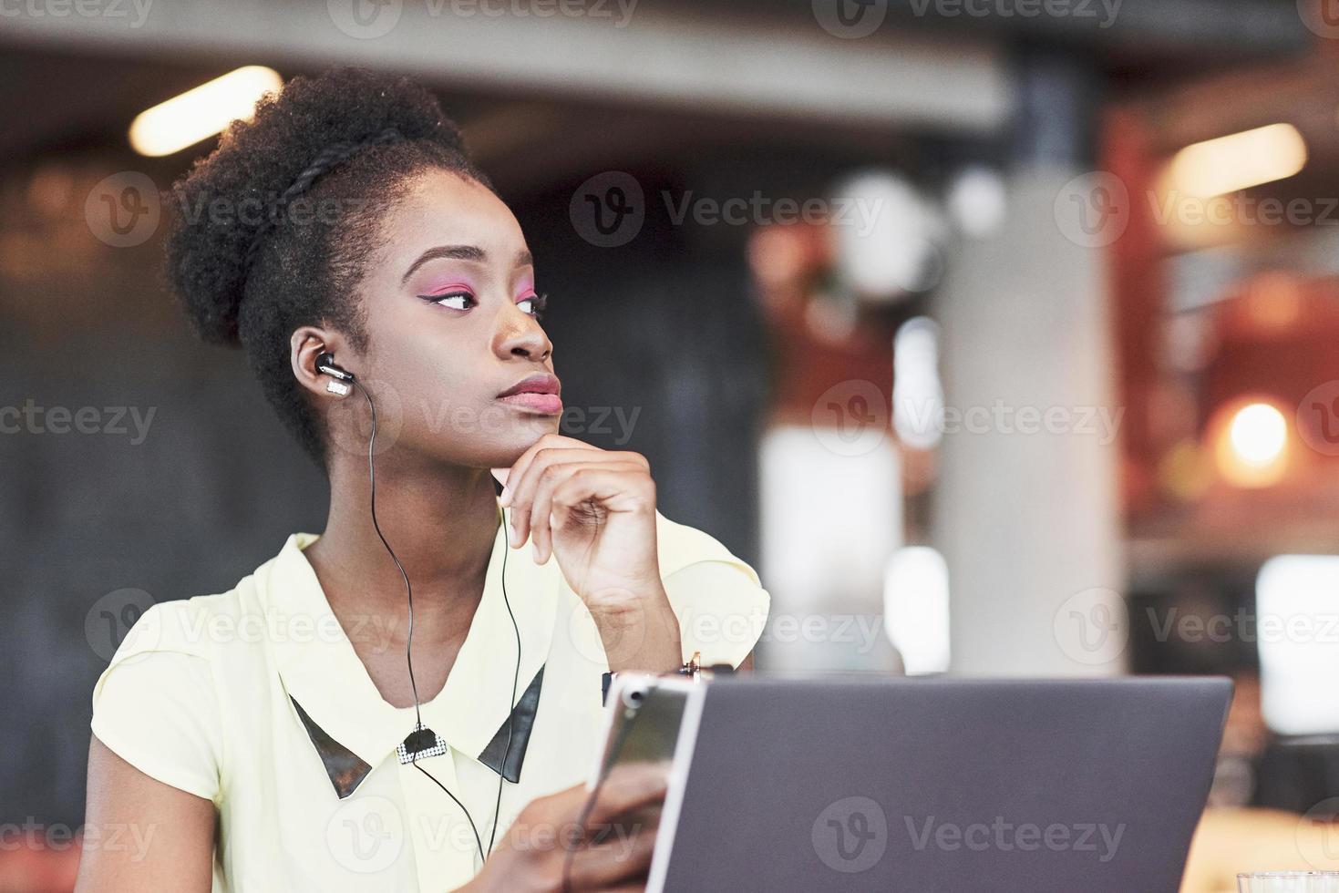 Ein junges afroamerikanisches Mädchen mit dunklen Locken, das in einem Café über einen Laptop nachdenkt foto