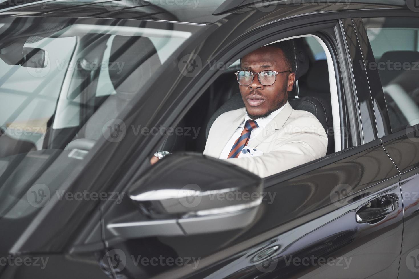 Vorderansicht des hübschen afrikanischen eleganten ernsten Geschäftsmannes fährt ein Auto foto