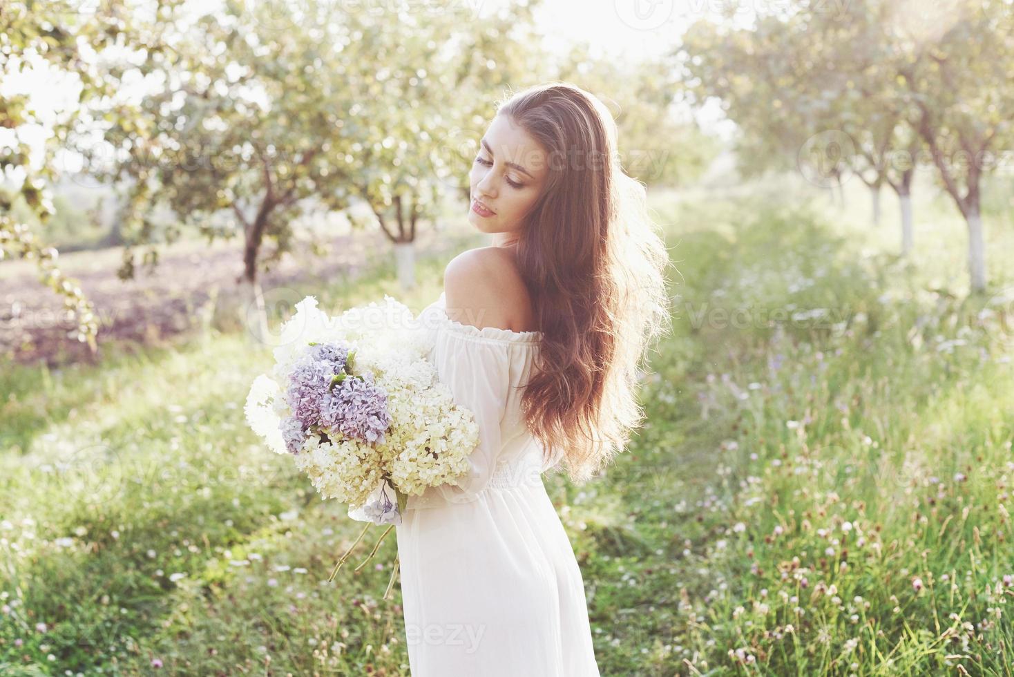 schöne junge frau, die ein elegantes weißes kleid trägt und einen schönen sonnigen nachmittag in einem sommergarten genießt foto