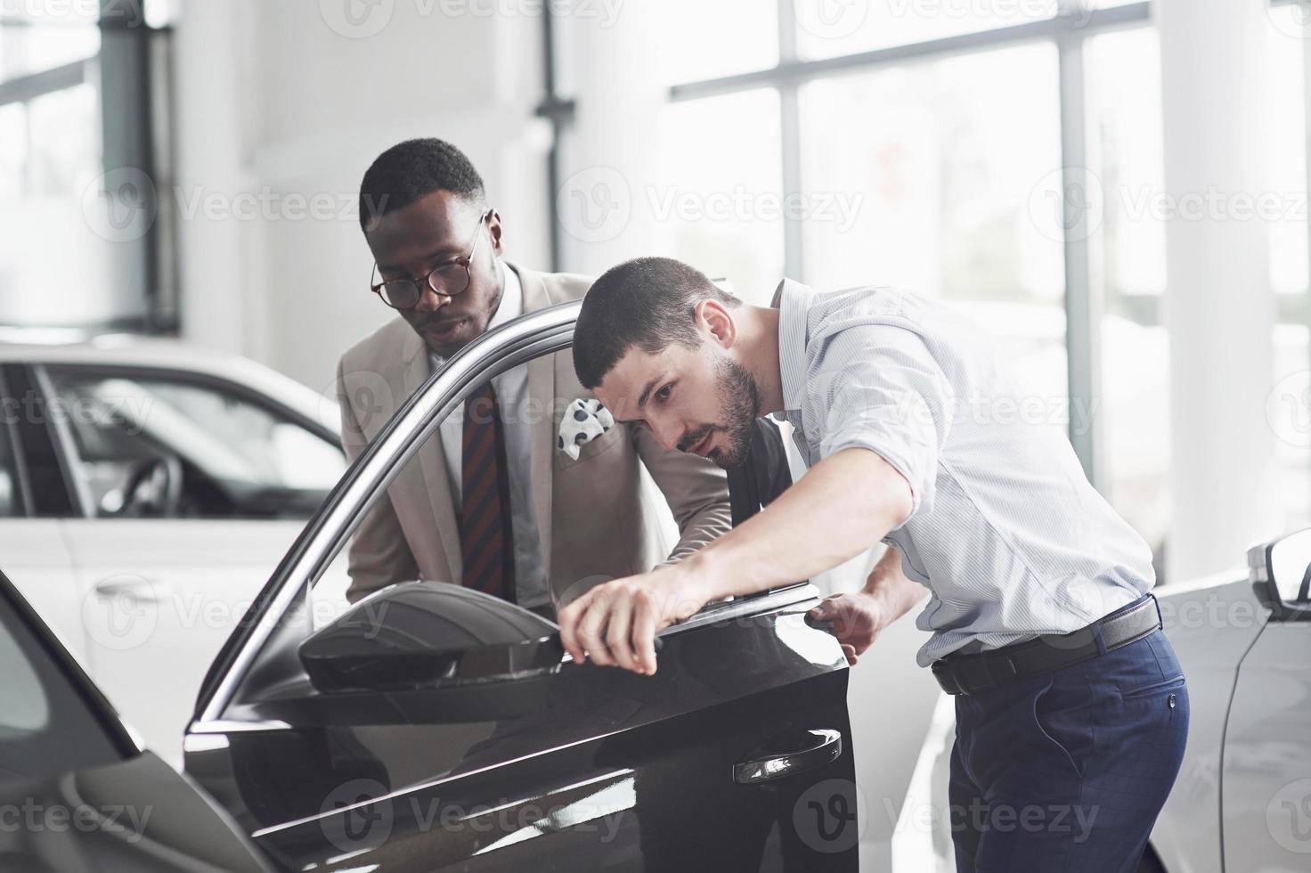 Ein afrikanischer Mann, der ein neues Auto kauft, überprüft ein Auto im Gespräch mit einem professionellen Verkäufer. foto
