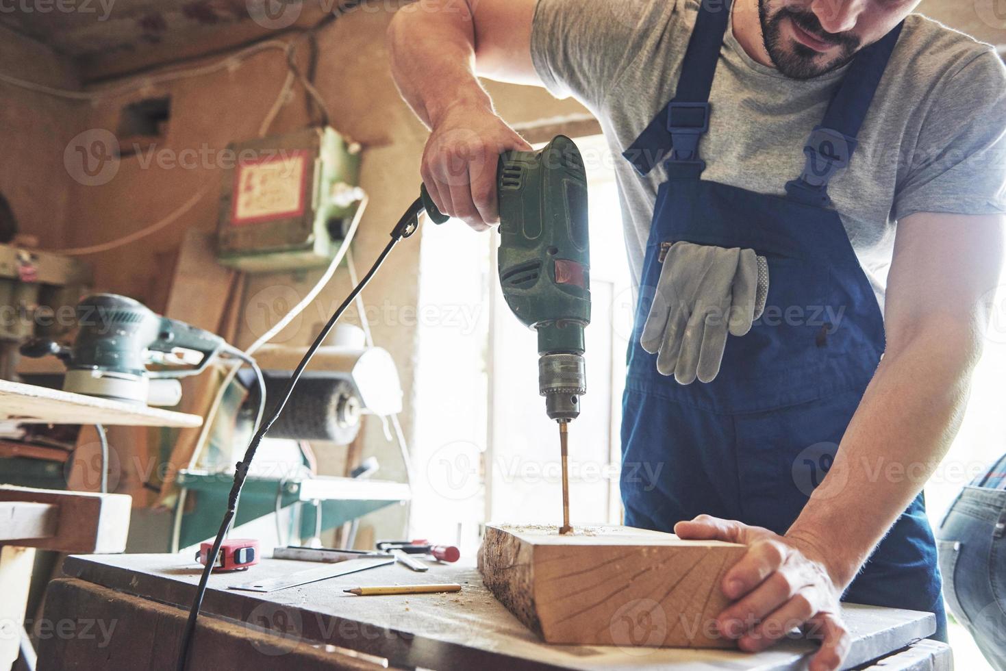 der Meister arbeitet in einem Atelier und bohrt ein Loch in ein Holzbrett. foto