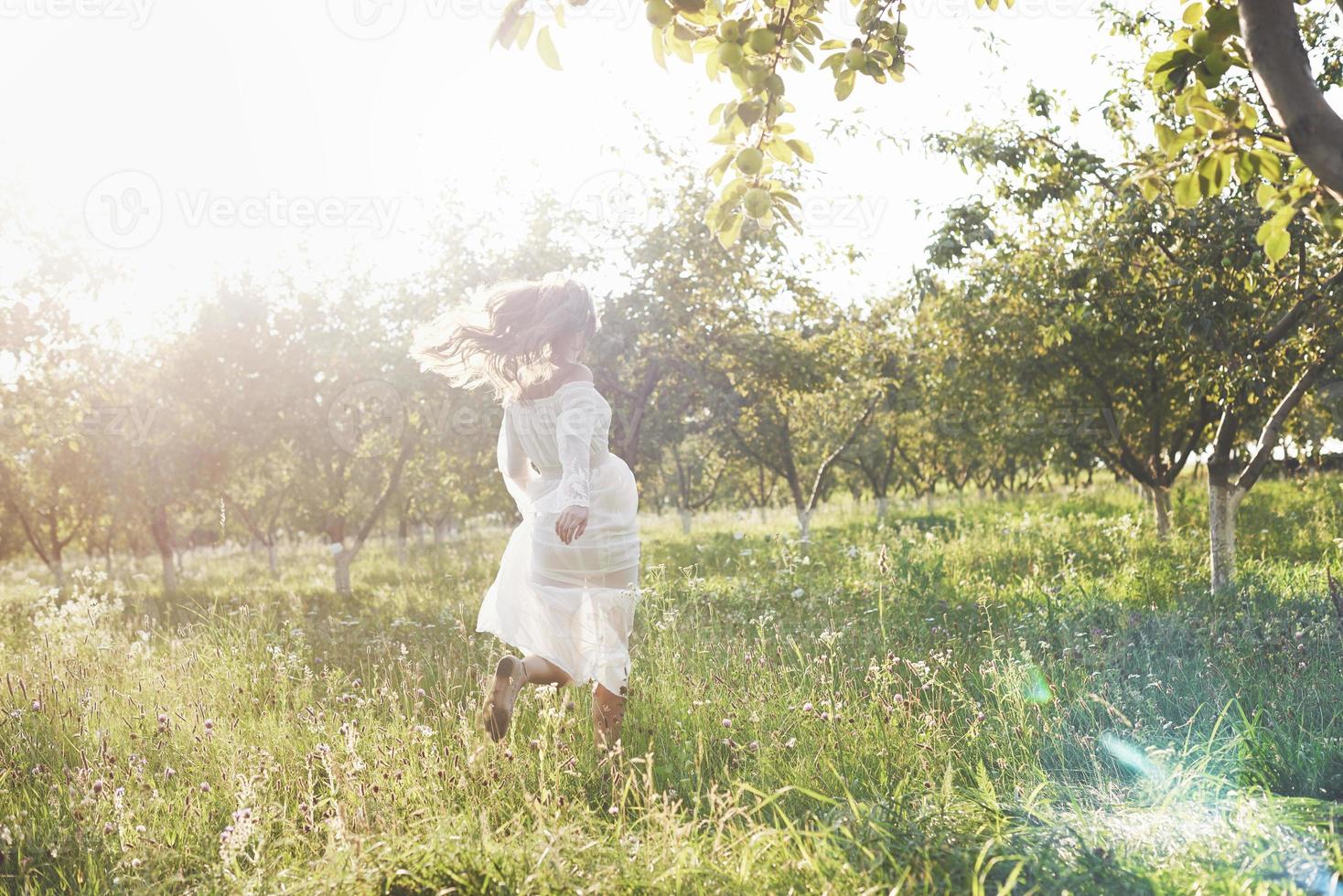 schöne junge frau, die ein elegantes weißes kleid trägt und einen schönen sonnigen nachmittag in einem sommergarten genießt foto