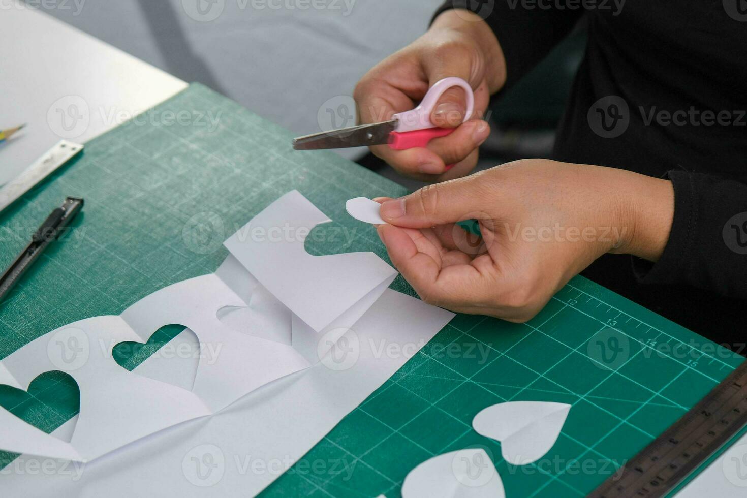 ein Frau schneidet aus ein Weiß herzförmig Papier mit Schere zu schmücken. Valentinstag Tag Gruß Karte oder Urlaub Geschenk Konzept. foto