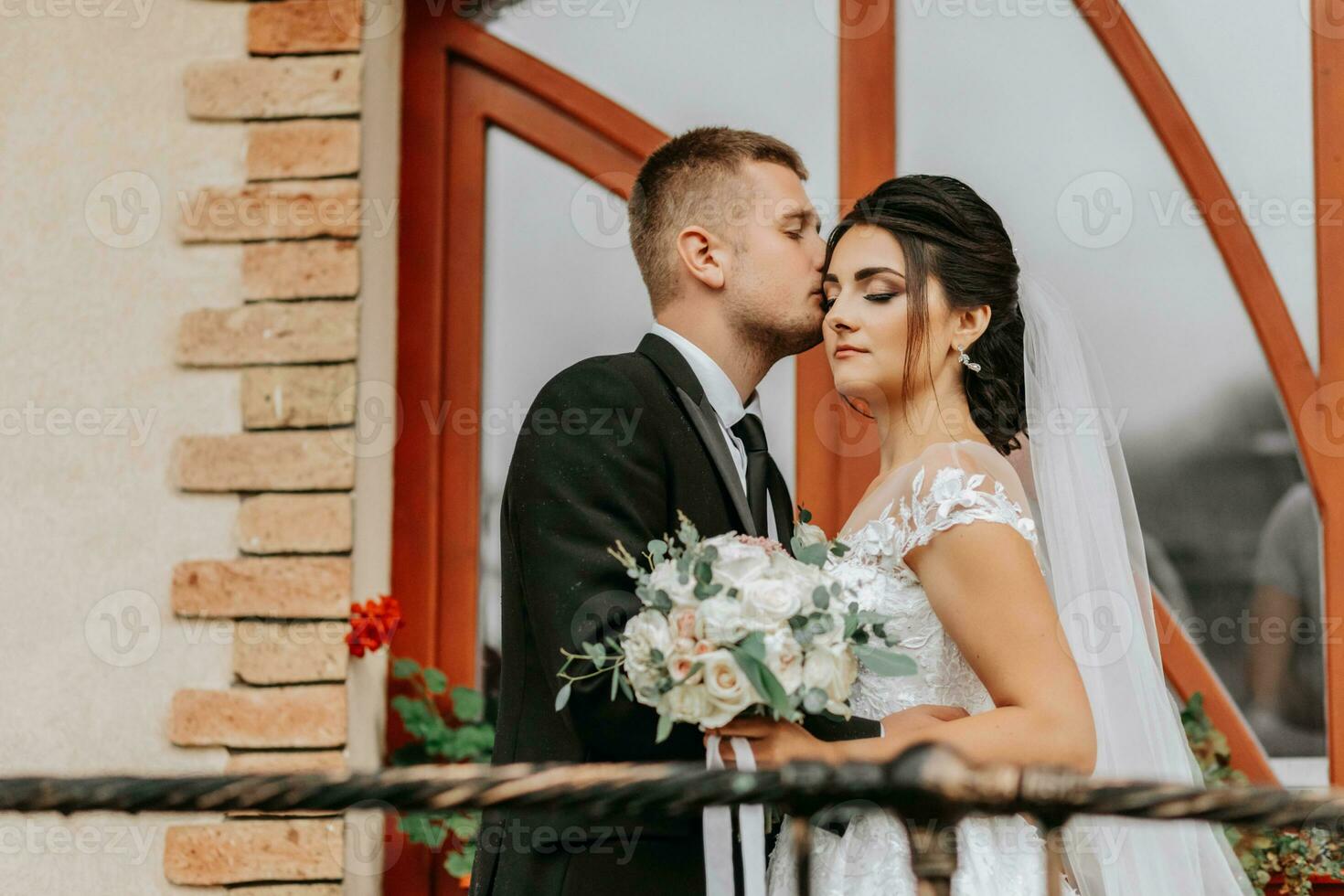 Porträt von das Braut und Bräutigam gegen das Hintergrund von das Fenster von ein alt authentisch Haus, Umarmungen und Küsse. kostenlos Raum. Hochzeit gehen im das Park foto