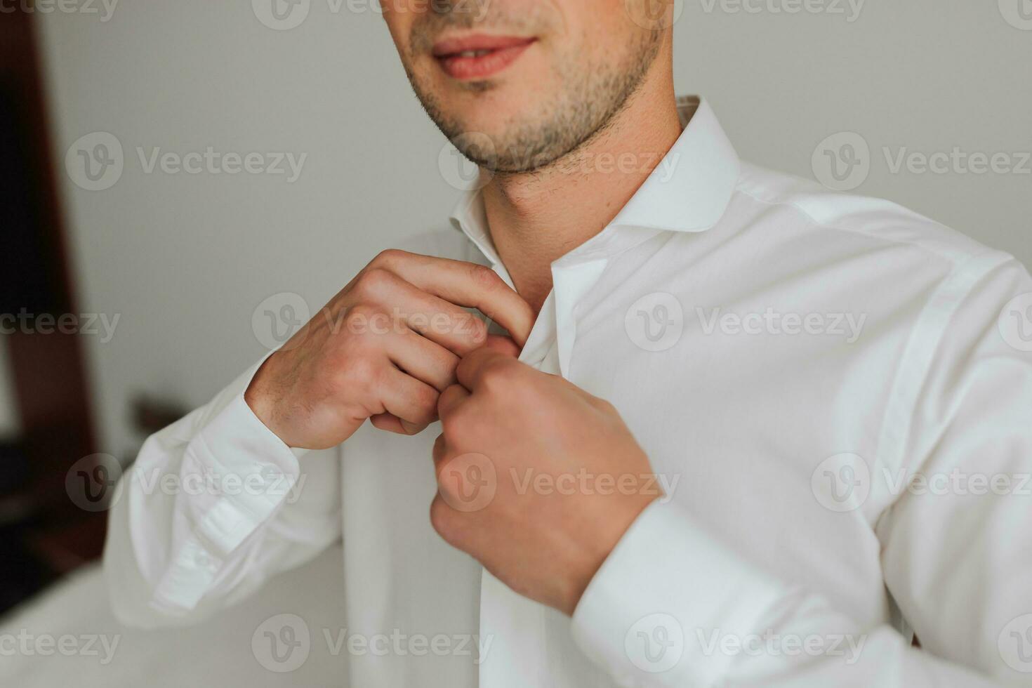 ein jung Mann im schwarz Hose setzt auf ein Weiß Hemd im seine Zimmer. das Bräutigam ist vorbereiten zum das Hochzeit Zeremonie. detailliert Nahansicht Foto von Hände