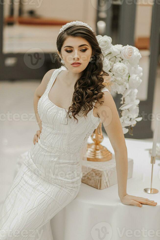 Studio Foto von ein Mädchen im ein Hochzeit Kleid, posieren in der Nähe von ein Tabelle mit Blumen