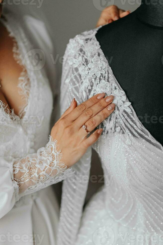 Einzelheiten Hochzeit Zubehör. ein Brünette Braut berührt ihr Kleid mit ihr Hand. abgeschnitten Foto. schön Hände. öffnen Büste foto