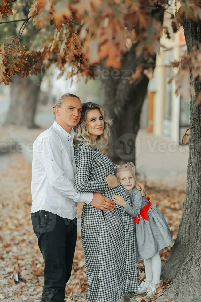 Porträt von ein jung schwanger Frau mit ihr Familie draußen im ein Park unter vergilbt Blätter foto