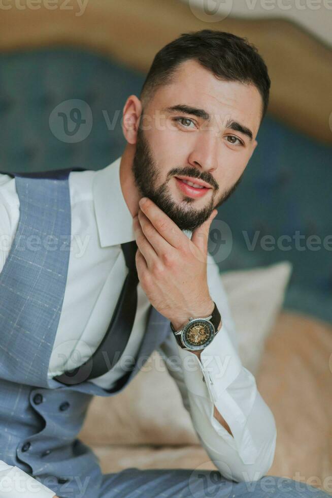 Porträt von ein stilvoll Mann mit ein schwarz Bart im ein Shirt, Weste und binden, mit ein stark Uhr auf seine Hand foto