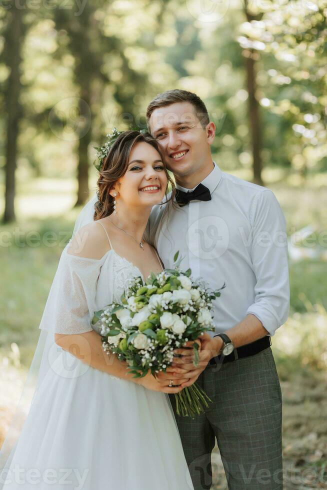 modisch Bräutigam und süß Braut im Weiß Kleid mit Tiara von frisch Blumen, umarmen, Lachen im Park, Garten, Wald draußen. Hochzeit Fotografie, Porträt von lächelnd Jungvermählten. foto