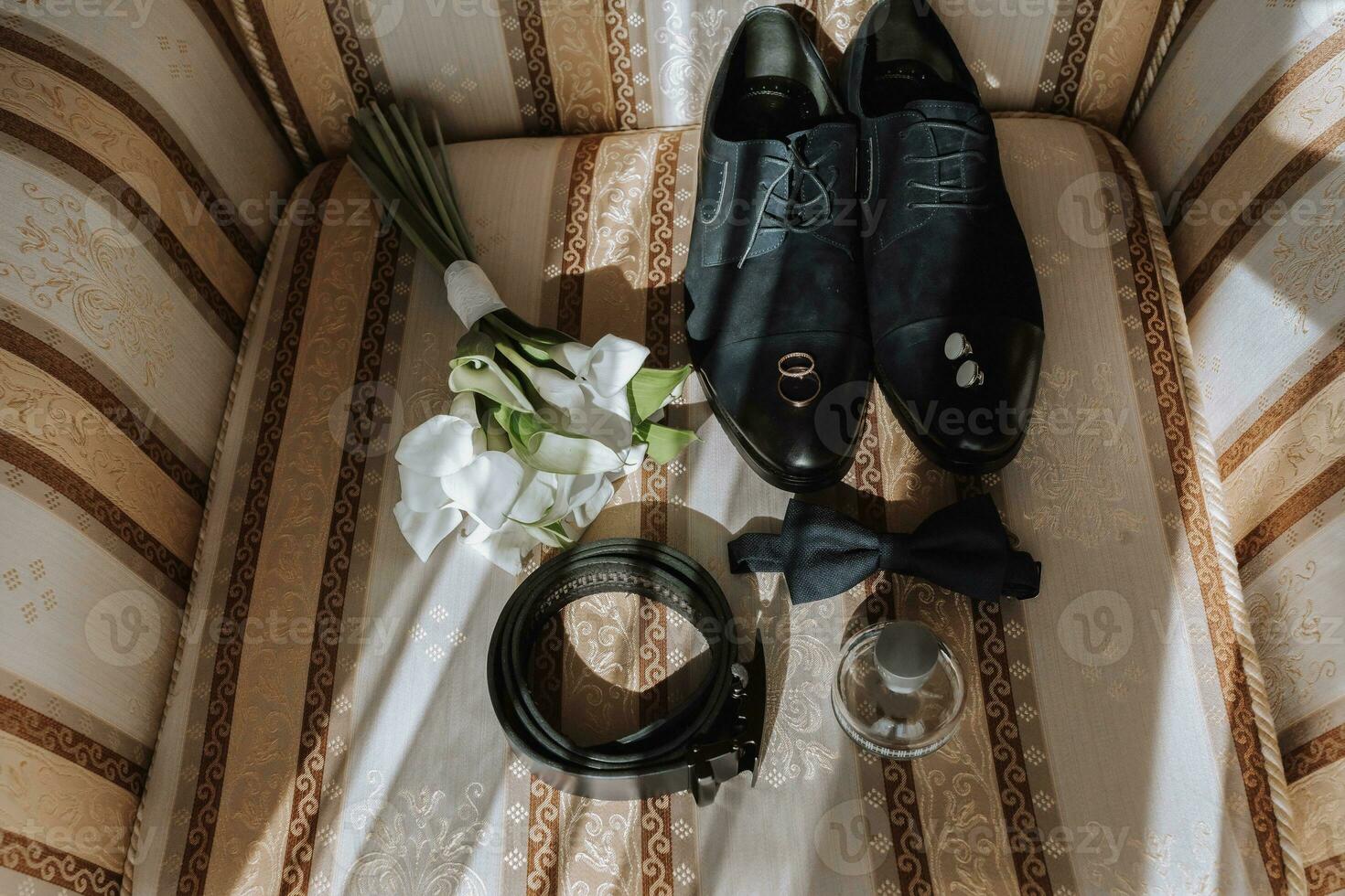 Einzelheiten von das Bräutigam auf das Stuhl. schwarz Velours Stiefel, Gold Hochzeit Ringe, Herren Parfüm, Manschettenknöpfe, ein Strauß von Calla Blumen foto