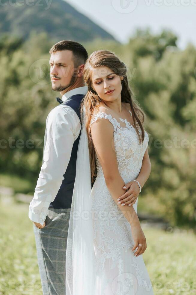 Porträt von ein stilvoll Bräutigam und Braut gegen das Hintergrund von Sommer- Berge. das Konzept von ein rustikal Hochzeit im das Berge, glücklich Bohemien Jungvermählten. foto