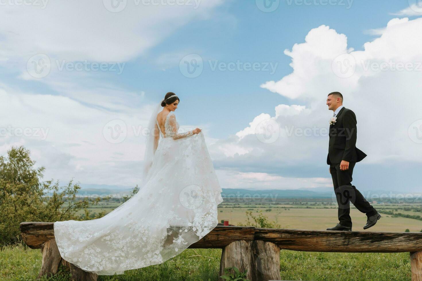 stilvoll Braut und Bräutigam Umarmung und Kuss gegen das Hintergrund von Sommer- Berge. das Konzept von ein rustikal Hochzeit im das Berge, glücklich Bohemien Jungvermählten. foto