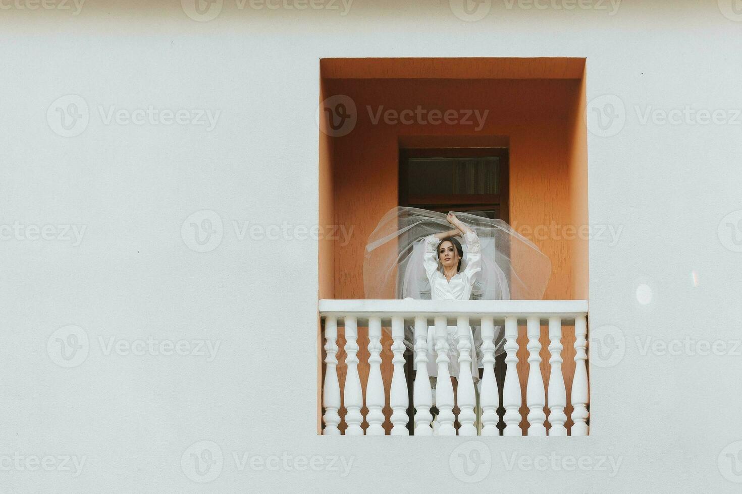 das Braut im ein Weiß Kleid, Stehen auf das Balkon, wirft oben das Schleier. Vorderseite Foto. kostenlos Raum foto