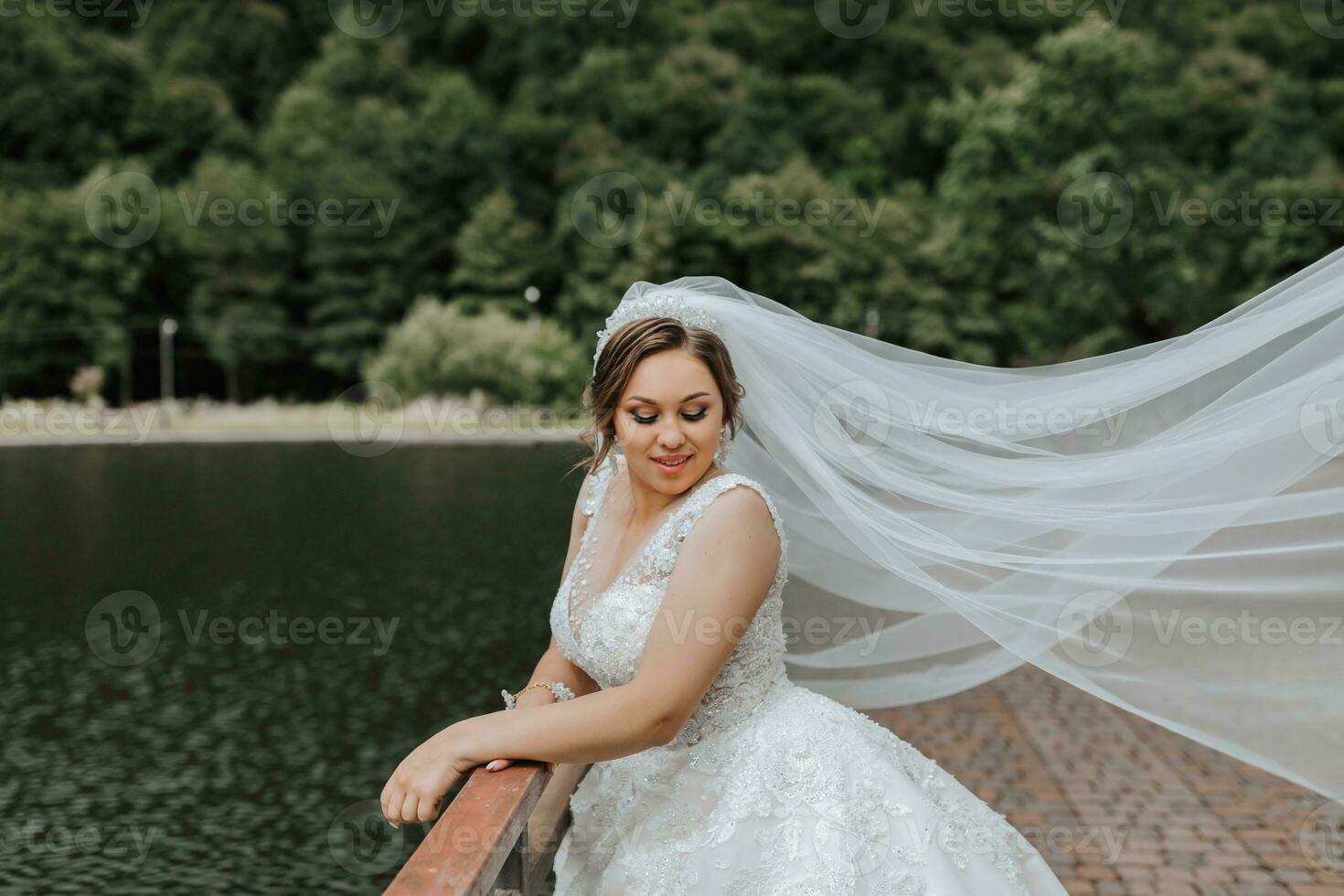 Hochzeit Porträt. das Braut im ein Weiß Kleid auf das Brücke mit ein fließend Schleier. aufrichtig lächeln. Wind und Schleier. Diadem. foto