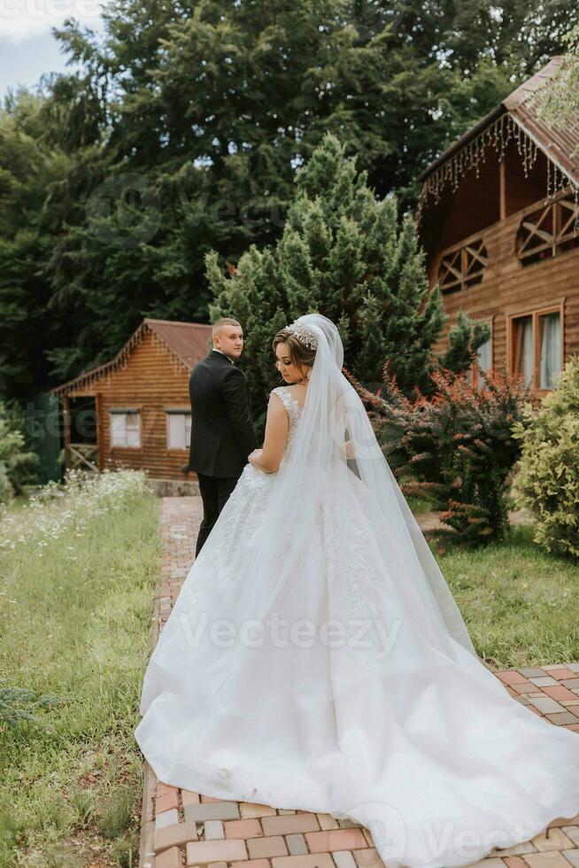 modisch Bräutigam und süß Braut im Weiß Kleid mit Krone, Bräutigam führt Braut durch Hand, Garten, Wald draußen. Hochzeit Fotografie, Porträt von lächelnd Jungvermählten. foto