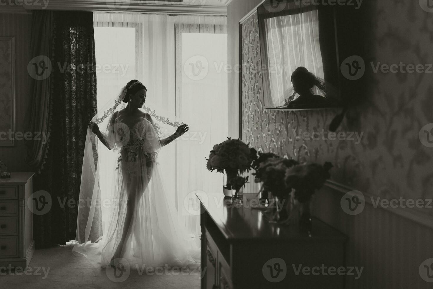 ein schön Mädchen mit ein Hochzeit Frisur und ein Tiara auf ihr Kopf im ein transparent Kleid ist vorbereiten zum ein Hochzeit im ein Hotel mit ein königlich Innere. foto