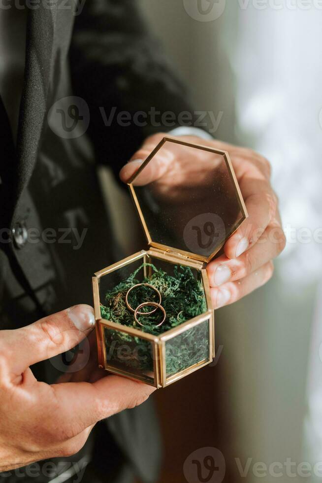 Hochzeit Ringe Lüge im ein schön Glas Box auf Grün Moos. Einzelheiten von das Verb während das Morgen Treffen foto