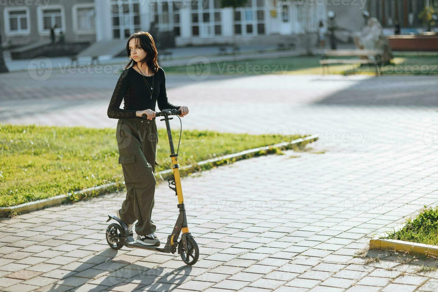 draussen Porträt von jung Teenager Brünette Mädchen mit lange Haar Fahren Roller auf Stadt Straße foto