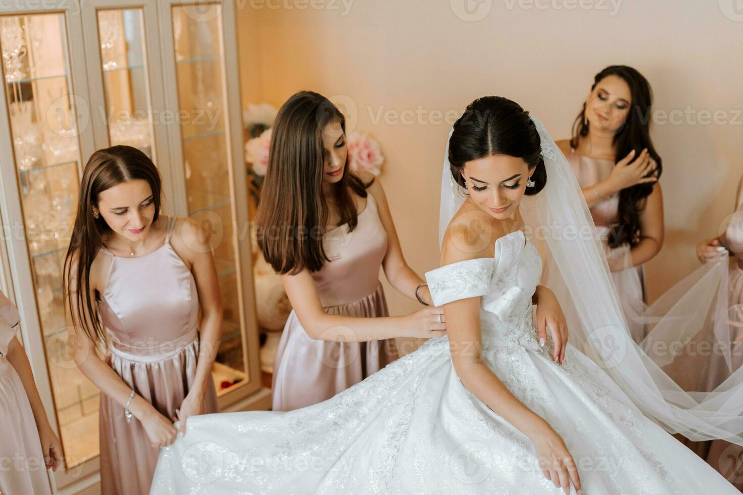 stilvoll schön Brautjungfern im passend Seide Kleider Portion Herrlich Brünette Braut im Weiß Kleid erhalten bereit zum Hochzeit, Morgen Vorbereitungen, Frau Putten auf Kleid foto