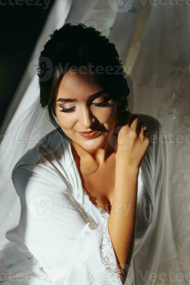 Porträt von ein Mädchen im ein Morgen Kleid. glücklich Braut mit Fachmann bilden und lange Schleier posieren zum Fotograf. das Braut ist vorbereiten zum das Hochzeit foto