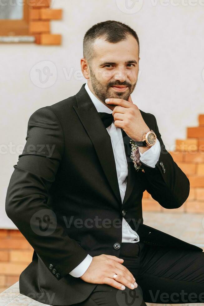 gut aussehend bärtig Mann Bräutigam im schwarz passen und schwarz Bogen Krawatte Stehen draußen. Hochzeit Porträt. ein Mann im ein klassisch passen foto