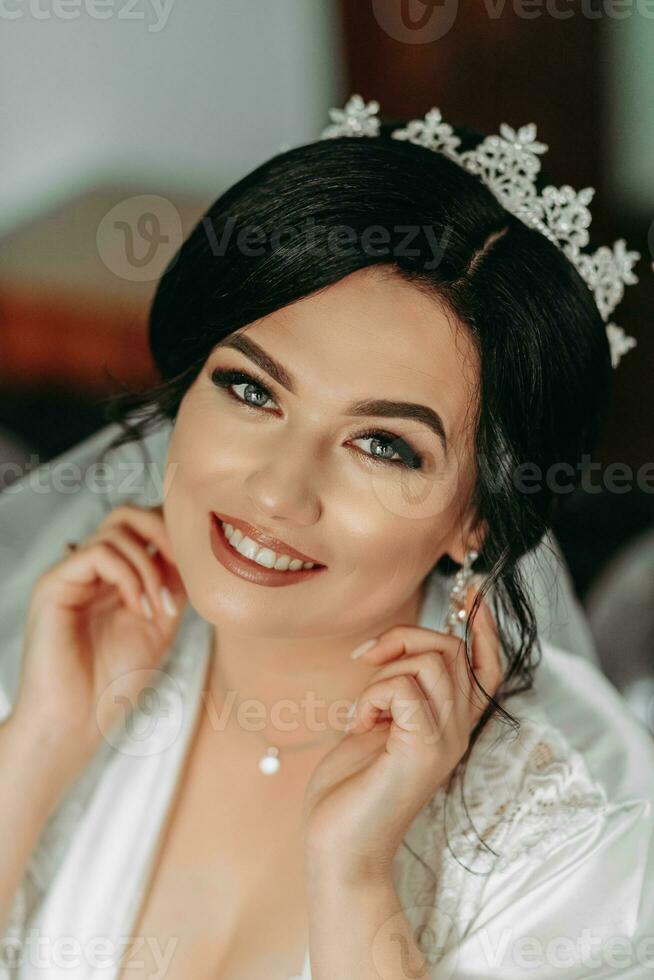 Porträt von ein Braut im ein Weiß Kleid mit ein schön Frisur und ein Krone auf ihr Kopf, suchen beim das Kamera. sinnlich süß Braut posieren. das Konzept von Luxus unter modisch Stil. foto