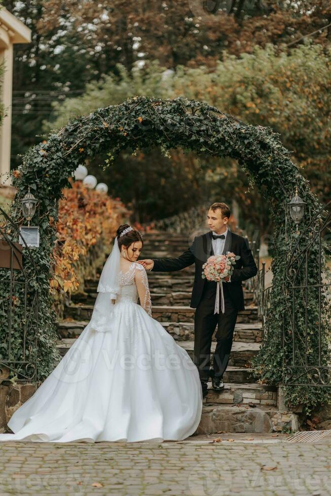 ein glücklich Paar von stilvoll Jungvermählten im ein Grün Park auf ein Herbst Tag. das Braut im ein lange Weiß Kleid und das Bräutigam im ein schwarz Anzug. Porträt von das Braut und Bräutigam auf ihr Hochzeit Tag. foto