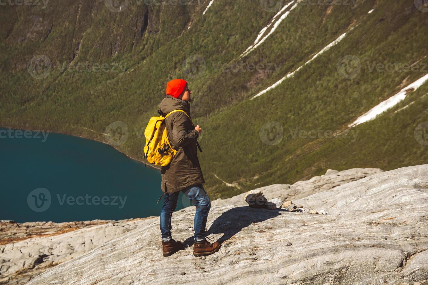 Mann mit einem Rucksack, der auf einem Felsen vor dem Hintergrund von Berg und See steht foto