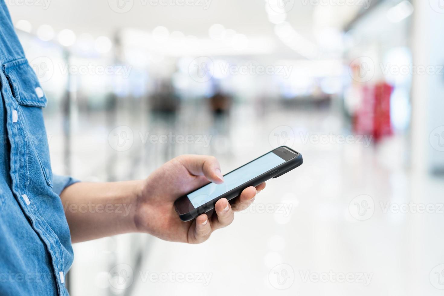 Mannhand, die mobiles Smartphone mit leerem Bildschirm auf unscharfem Hintergrund des Einkaufszentrums hält. foto