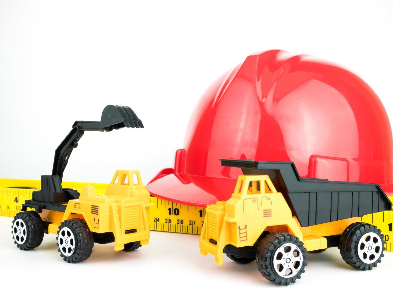 roter Schutzhelm mit mechanischem Bagger und LKW-Spielzeug, Ingenieurbaukonzept foto